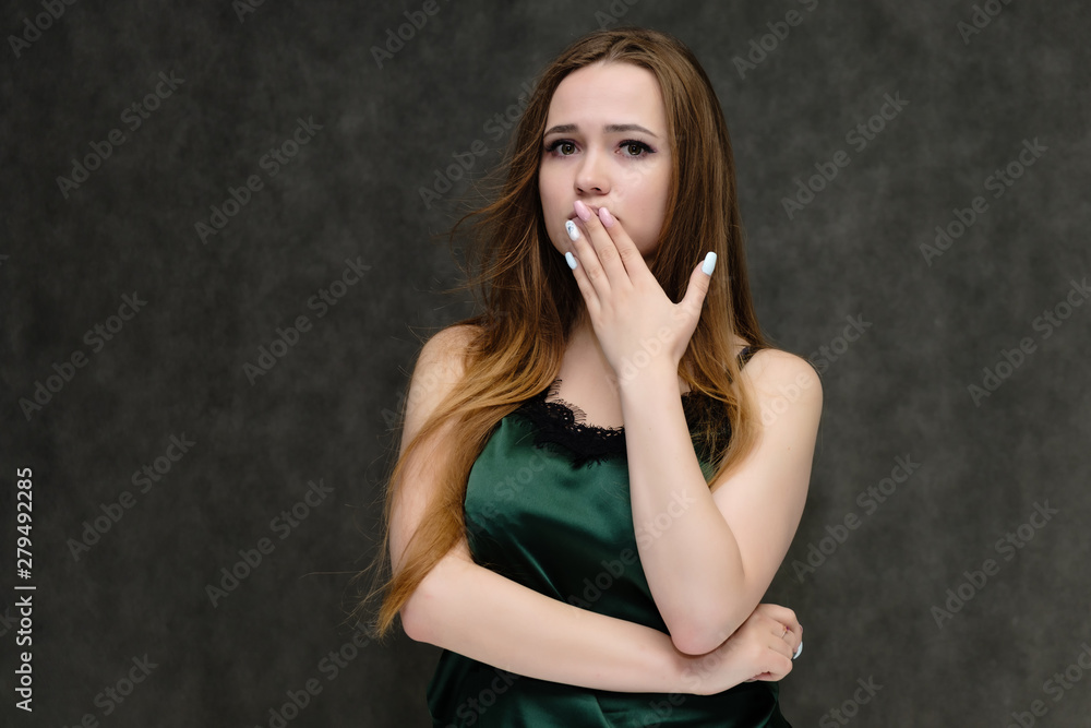 Concept portrait of the waist of a pretty girl, a young woman with long beautiful brown hair and a green T-shirt on a gray background. In the studio in different poses showing emotions. Concept portrait of the waist of a pretty girl, a young woman with long beautiful brown hair and a green T-shirt on a gray background. In the studio in different poses showing emotions.