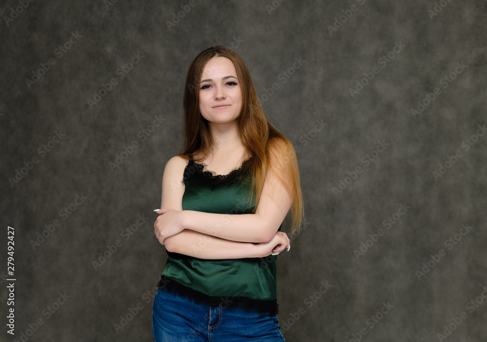 Concept portrait below belt of pretty girl, young woman with long beautiful brown hair and green t-shirt and blue jeans on gray background. In the studio in different poses showing emotions. Concept portrait below belt of pretty girl, young woman with long beautiful brown hair and green t-shirt and blue jeans on gray background. In the studio in different poses showing emotions.