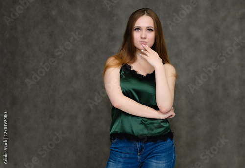 Concept portrait below belt of pretty girl, young woman with long beautiful brown hair and green t-shirt and blue jeans on gray background. In the studio in different poses showing emotions.