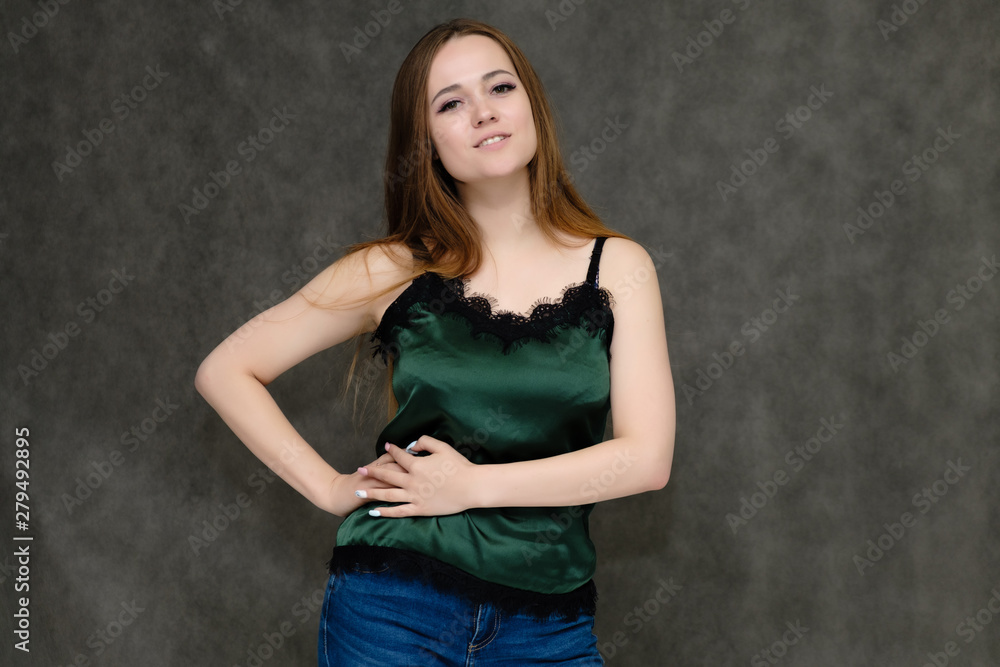 Concept portrait below belt of pretty girl, young woman with long beautiful brown hair and green t-shirt and blue jeans on gray background. In the studio in different poses showing emotions. Concept portrait below belt of pretty girl, young woman with long beautiful brown hair and green t-shirt and blue jeans on gray background. In the studio in different poses showing emotions.