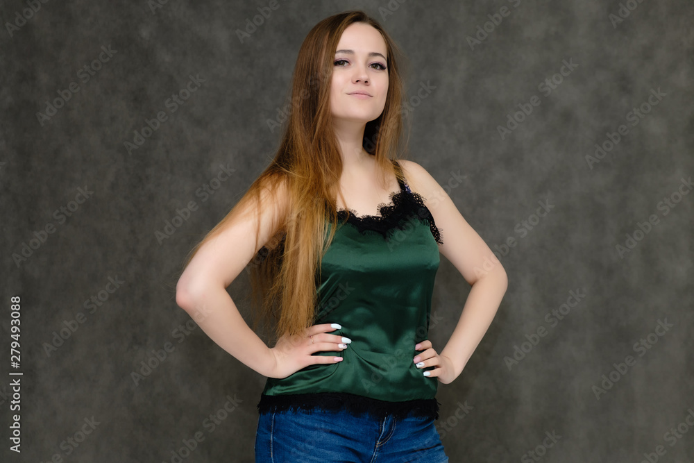 Concept portrait below belt of pretty girl, young woman with long beautiful brown hair and green t-shirt and blue jeans on gray background. In the studio in different poses showing emotions. Concept portrait below belt of pretty girl, young woman with long beautiful brown hair and green t-shirt and blue jeans on gray background. In the studio in different poses showing emotions.