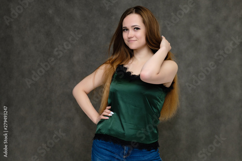 Concept portrait below belt of pretty girl, young woman with long beautiful brown hair and green t-shirt and blue jeans on gray background. In the studio in different poses showing emotions.