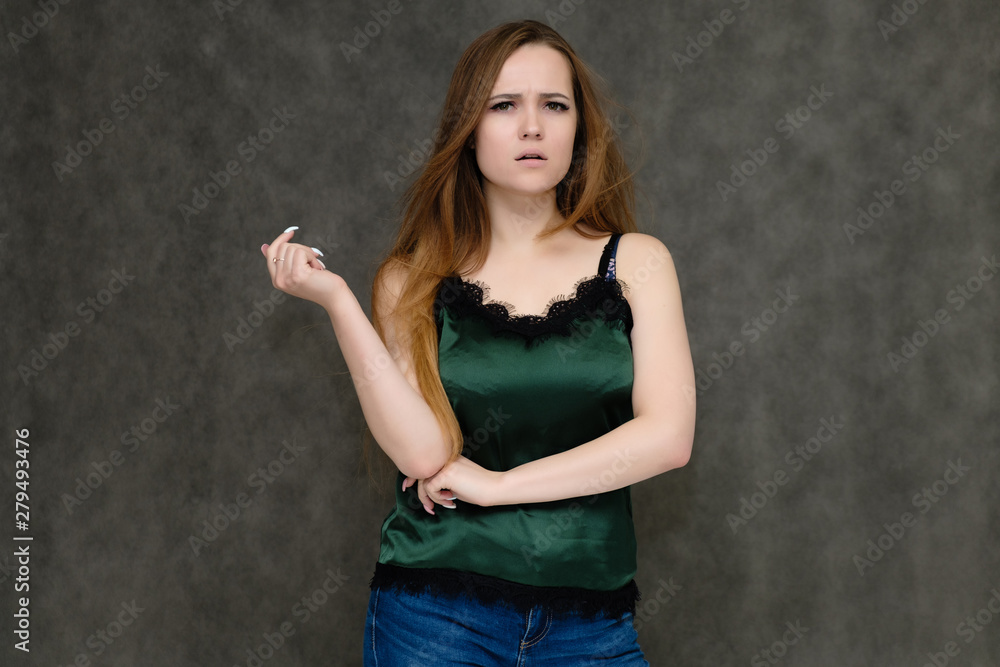 Concept portrait below belt of pretty girl, young woman with long beautiful brown hair and green t-shirt and blue jeans on gray background. In the studio in different poses showing emotions. Concept portrait below belt of pretty girl, young woman with long beautiful brown hair and green t-shirt and blue jeans on gray background. In the studio in different poses showing emotions.