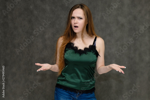 Concept portrait below belt of pretty girl, young woman with long beautiful brown hair and green t-shirt and blue jeans on gray background. In the studio in different poses showing emotions.