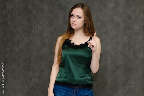 Concept portrait below belt of pretty girl, young woman with long beautiful brown hair and green t-shirt and blue jeans on gray background. In the studio in different poses showing emotions. © Вячеслав Чичаев