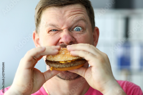 Funny bearded man with idiot facial expression eating big burger