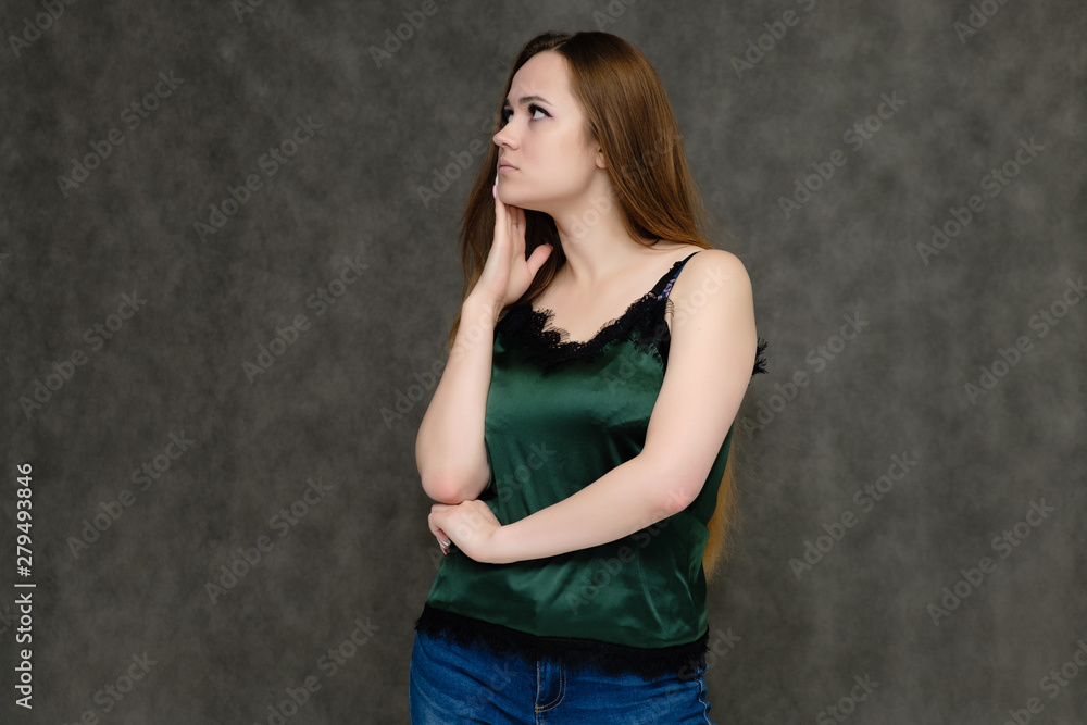 Concept portrait below belt of pretty girl, young woman with long beautiful brown hair and green t-shirt and blue jeans on gray background. In the studio in different poses showing emotions. Concept portrait below belt of pretty girl, young woman with long beautiful brown hair and green t-shirt and blue jeans on gray background. In the studio in different poses showing emotions.