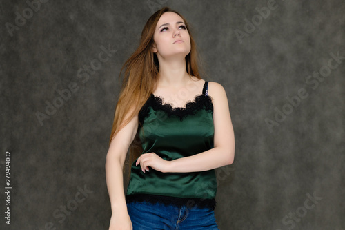 Concept portrait below belt of pretty girl, young woman with long beautiful brown hair and green t-shirt and blue jeans on gray background. In the studio in different poses showing emotions.