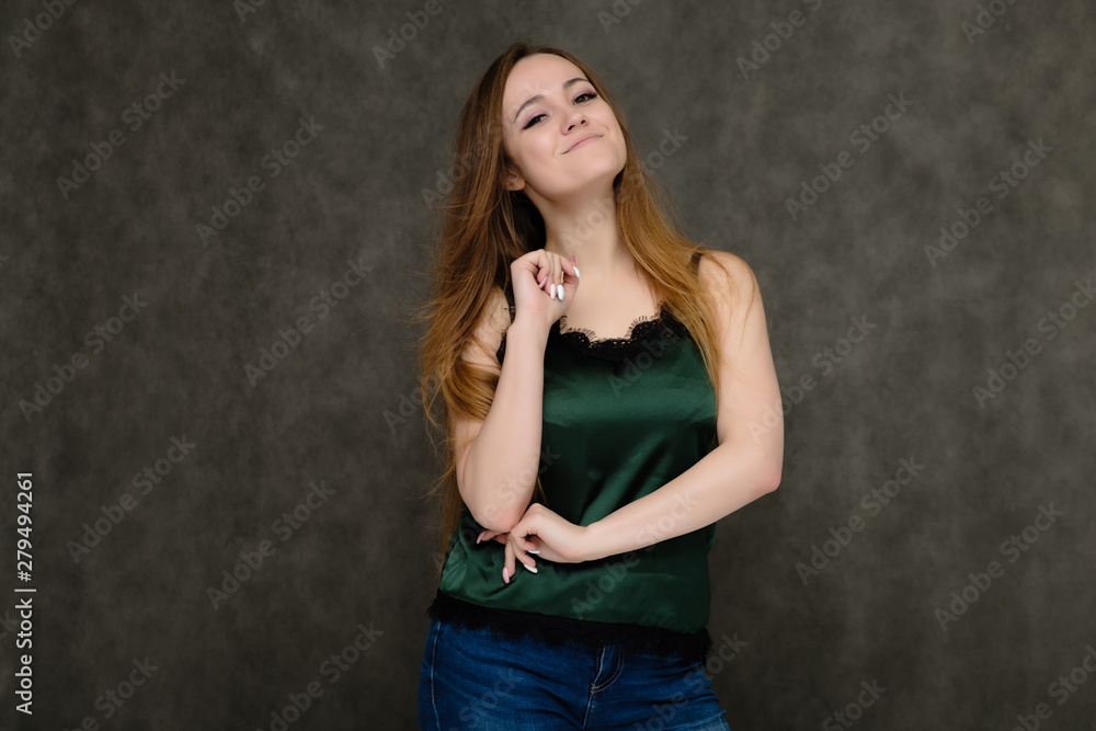 Concept portrait below belt of pretty girl, young woman with long beautiful brown hair and green t-shirt and blue jeans on gray background. In the studio in different poses showing emotions.