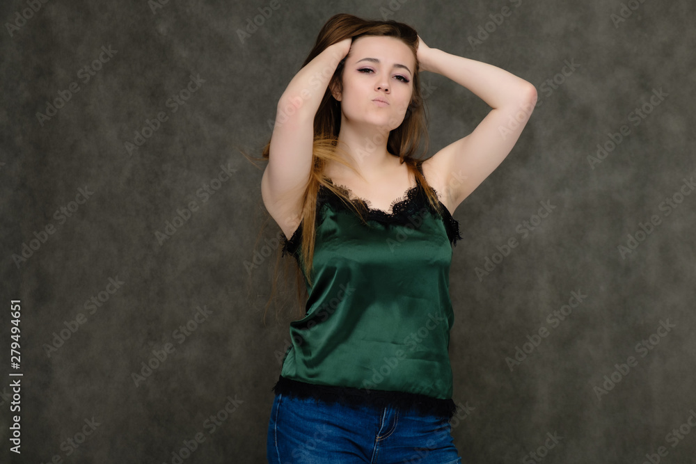 Naklejka premium Concept portrait below belt of pretty girl, young woman with long beautiful brown hair and green t-shirt and blue jeans on gray background. In the studio in different poses showing emotions.