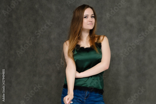 Concept portrait below belt of pretty girl, young woman with long beautiful brown hair and green t-shirt and blue jeans on gray background. In the studio in different poses showing emotions.