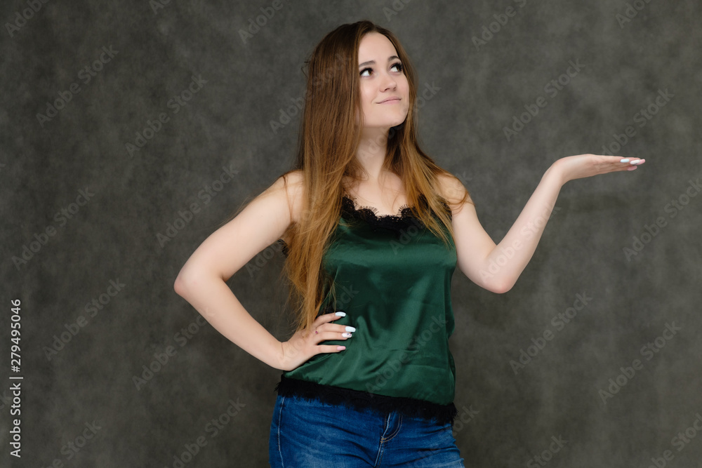 Concept portrait below belt of pretty girl, young woman with long beautiful brown hair and green t-shirt and blue jeans on gray background. In the studio in different poses showing emotions. Concept portrait below belt of pretty girl, young woman with long beautiful brown hair and green t-shirt and blue jeans on gray background. In the studio in different poses showing emotions.