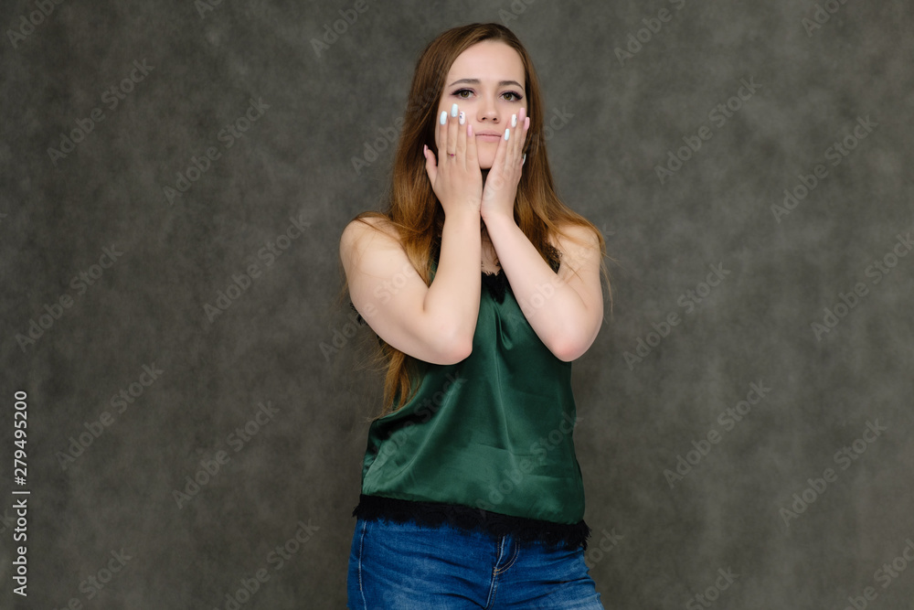 Concept portrait below belt of pretty girl, young woman with long beautiful brown hair and green t-shirt and blue jeans on gray background. In the studio in different poses showing emotions. Concept portrait below belt of pretty girl, young woman with long beautiful brown hair and green t-shirt and blue jeans on gray background. In the studio in different poses showing emotions.