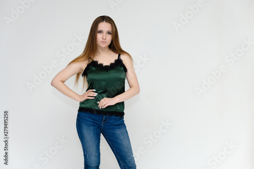 Concept portrait above the knee of a pretty girl, a young woman with long beautiful brown hair and a green t-shirt and blue jeans on a white background. In studio in different poses showing emotions.