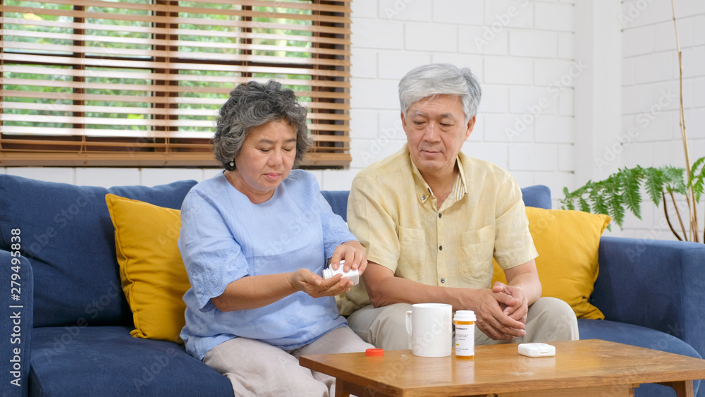 Obraz premium Senior asian couple take pill medicine for elderly health care while sitting on sofa, Retirement couple take vitamin pill, Senior asian medication and health care concept