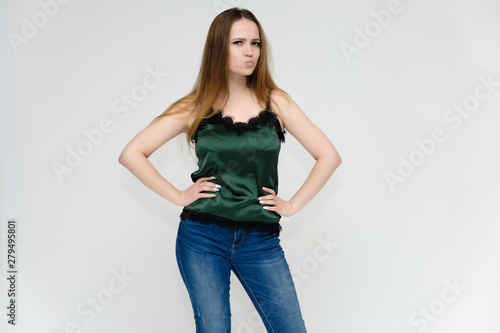 Concept portrait above the knee of a pretty girl, a young woman with long beautiful brown hair and a green t-shirt and blue jeans on a white background. In studio in different poses showing emotions.