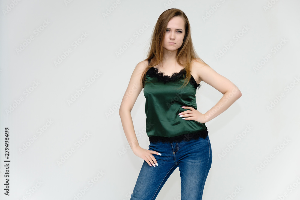 Concept portrait above the knee of a pretty girl, a young woman with long beautiful brown hair and a green t-shirt and blue jeans on a white background. In studio in different poses showing emotions. Concept portrait above the knee of a pretty girl, a young woman with long beautiful brown hair and a green t-shirt and blue jeans on a white background. In studio in different poses showing emotions.