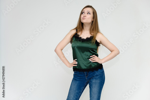 Concept portrait above the knee of a pretty girl, a young woman with long beautiful brown hair and a green t-shirt and blue jeans on a white background. In studio in different poses showing emotions.