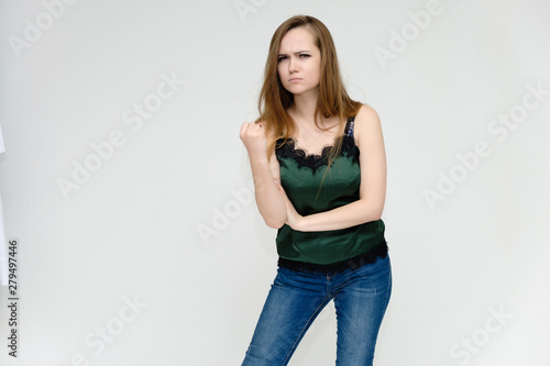 Concept portrait above the knee of a pretty girl, a young woman with long beautiful brown hair and a green t-shirt and blue jeans on a white background. In studio in different poses showing emotions.