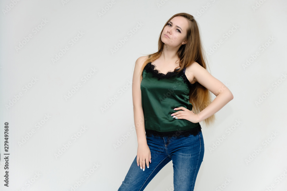 Concept portrait above the knee of a pretty girl, a young woman with long beautiful brown hair and a green t-shirt and blue jeans on a white background. In studio in different poses showing emotions. Concept portrait above the knee of a pretty girl, a young woman with long beautiful brown hair and a green t-shirt and blue jeans on a white background. In studio in different poses showing emotions.