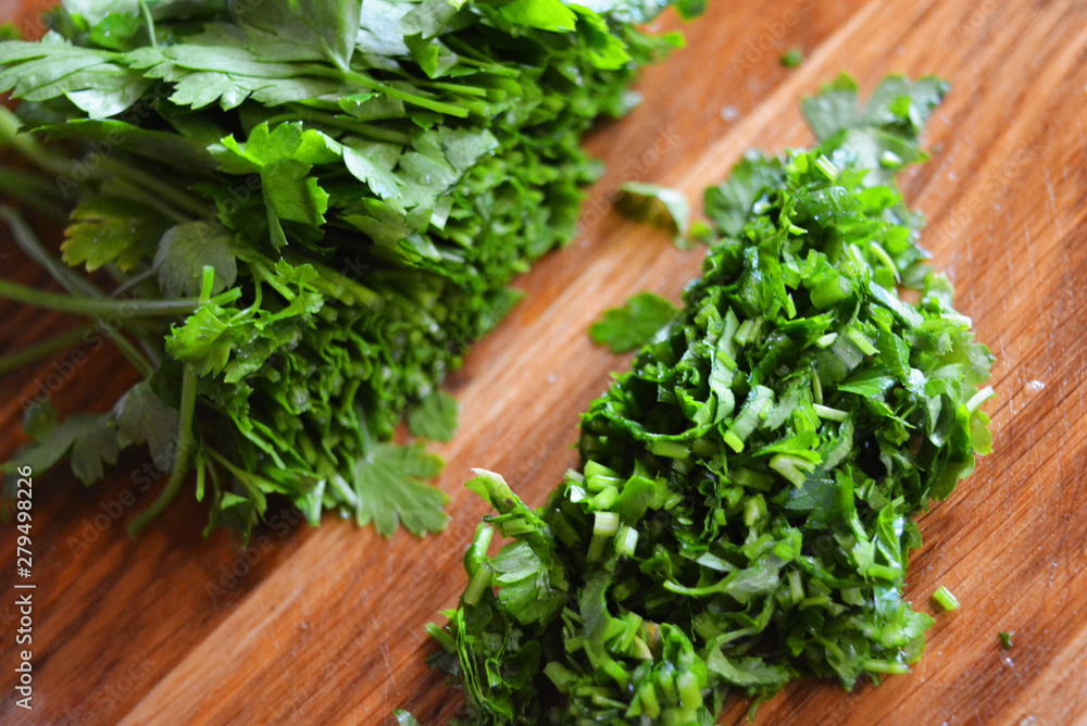 A bunch of green washed fresh parsley and chopped parsley for salad laid out on a wooden kitchen board.