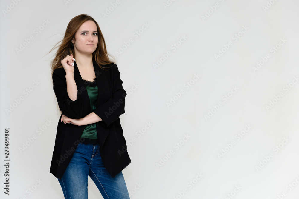 Concept portrait above the knee of a pretty girl, a young woman with long beautiful brown hair and a black jacket and blue jeans on a white background. In studio in different poses showing emotions. Concept portrait above the knee of a pretty girl, a young woman with long beautiful brown hair and a black jacket and blue jeans on a white background. In studio in different poses showing emotions.