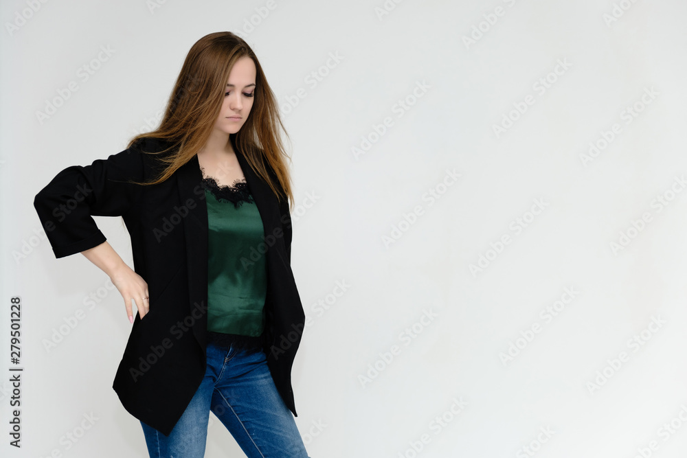 Concept portrait above the knee of a pretty girl, a young woman with long beautiful brown hair and a black jacket and blue jeans on a white background. In studio in different poses showing emotions. Concept portrait above the knee of a pretty girl, a young woman with long beautiful brown hair and a black jacket and blue jeans on a white background. In studio in different poses showing emotions.
