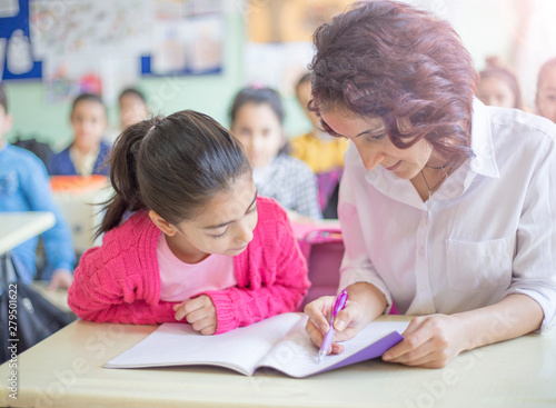 young female teacher helping her female student in classroom