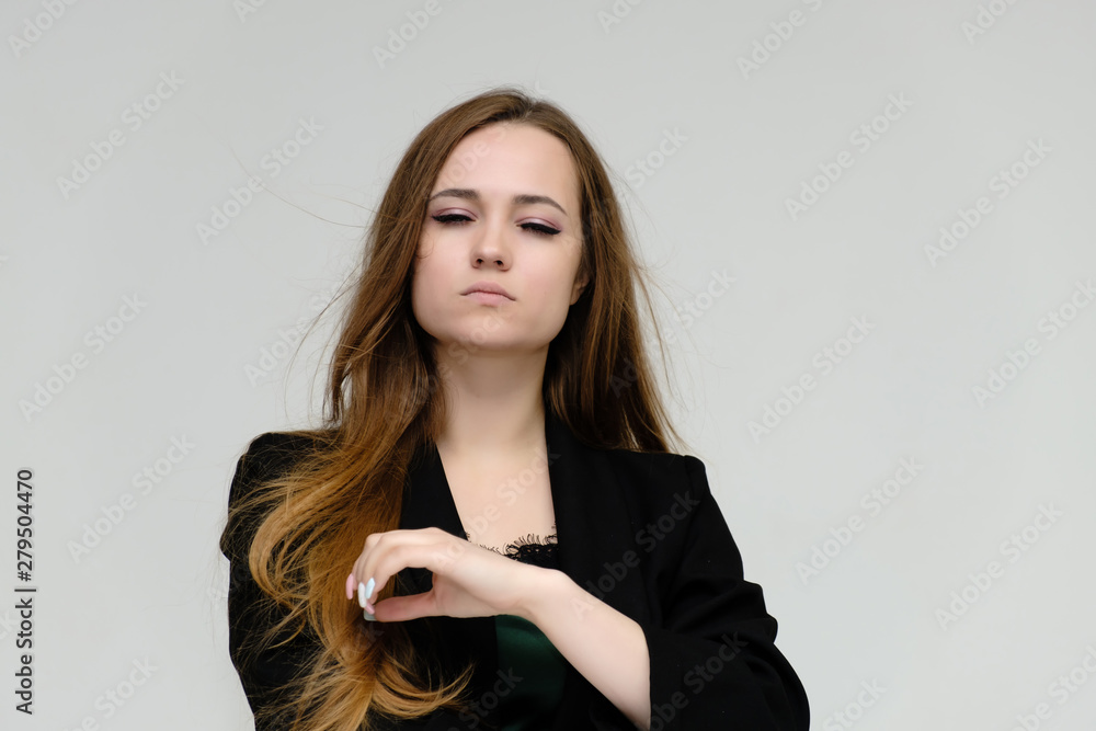 Concept close-up portrait of a pretty girl, a young woman with long beautiful brown hair and a black jacket on a white background. In the studio in different poses showing emotions. Concept close-up portrait of a pretty girl, a young woman with long beautiful brown hair and a black jacket on a white background. In the studio in different poses showing emotions.