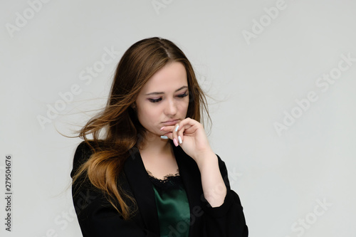Concept close-up portrait of a pretty girl, a young woman with long beautiful brown hair and a black jacket on a white background. In the studio in different poses showing emotions.