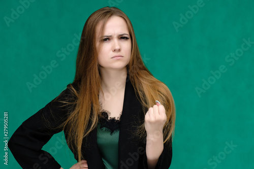 Concept close-up portrait of a pretty girl, a young woman with long beautiful brown hair and in a black jacket on a green background. In the studio in different poses showing emotions. © Вячеслав Чичаев