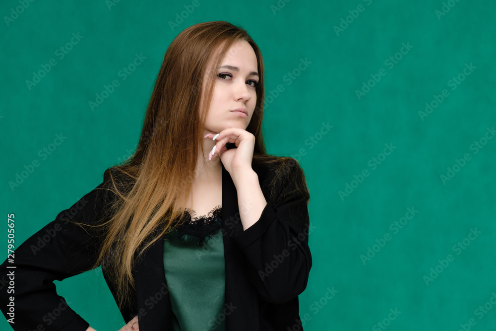 Concept close-up portrait of a pretty girl, a young woman with long beautiful brown hair and in a black jacket on a green background. In the studio in different poses showing emotions. Concept close-up portrait of a pretty girl, a young woman with long beautiful brown hair and in a black jacket on a green background. In the studio in different poses showing emotions.