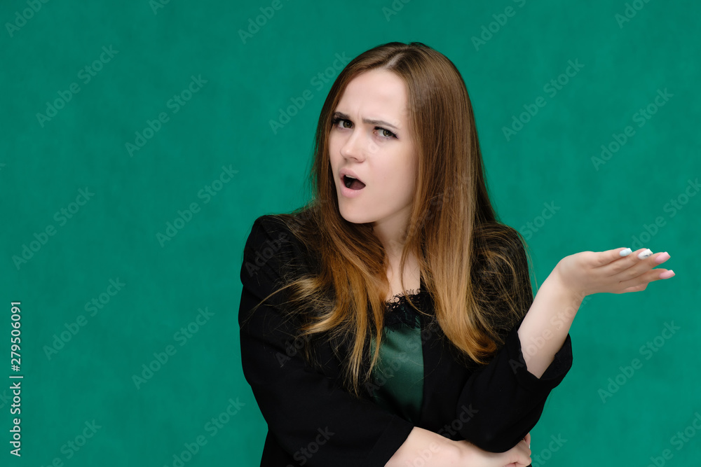 Concept close-up portrait of a pretty girl, a young woman with long beautiful brown hair and in a black jacket on a green background. In the studio in different poses showing emotions.