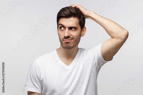 Young doubtful man thinking, scratching his head trying to find solution, isolated on gray background