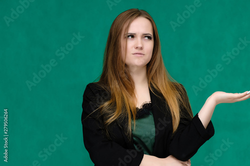 Concept close-up portrait of a pretty girl, a young woman with long beautiful brown hair and in a black jacket on a green background. In the studio in different poses showing emotions. © Вячеслав Чичаев