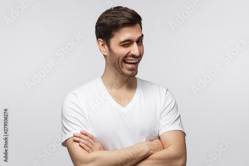 Young cheerful man winking while flirting, isolated on gray background