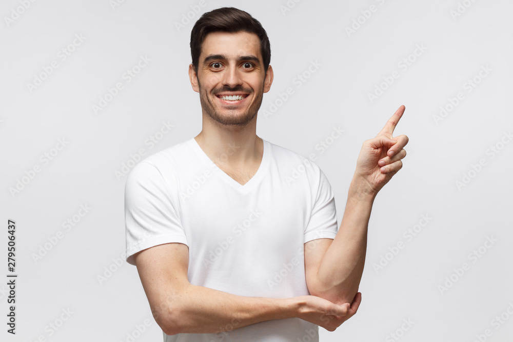 Handsome smiling man in white t-shirt pointing right with finger isolated on gray background