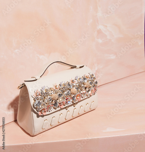 Pretty leather handbag standing on marble pink background. Crystal embellished feminine purse, coral peach pastel backdrop. Renovation concept. Fashion backlight. Copy space for your design
