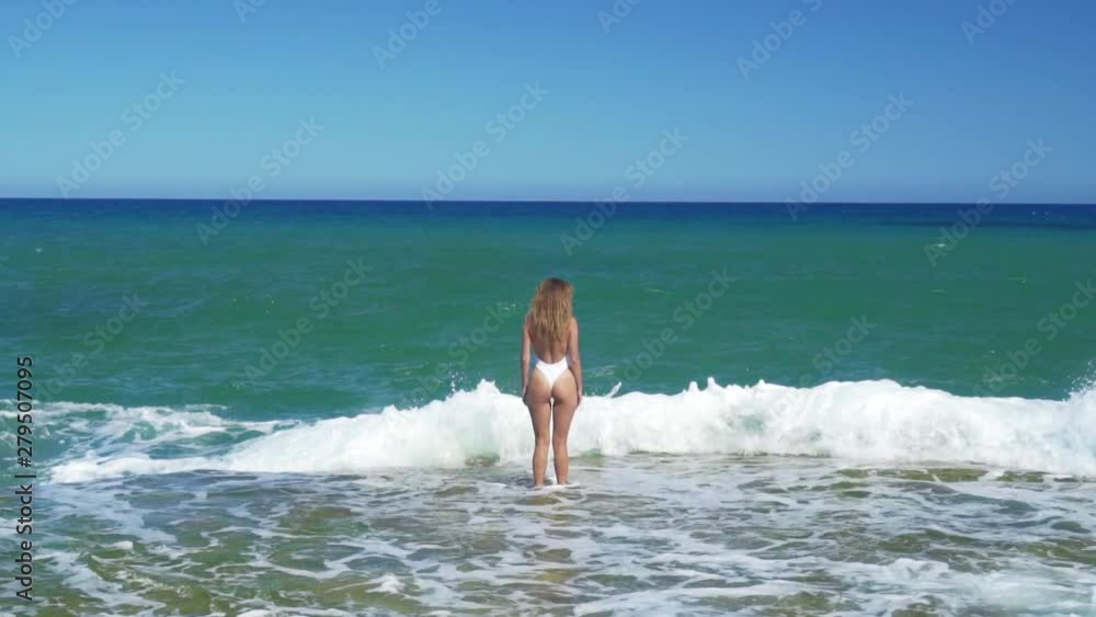 Young woman in bikini on sea shore and splashing water waves aerial landscape. Beautiful woman on rocky sea beach drone view. Young woman in bikini on sea shore and splashing water waves aerial landscape. Beautiful woman on rocky sea beach drone view.