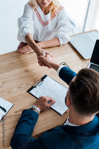 overhead view of recruiter and happy employee shaking hands in office