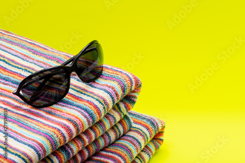 Folded Colorful Striped Organic Cotton Beach Towels and black Sunglasses on bright yellow background as Summer Vacation Theme.