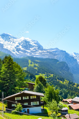 Stunning village Wengen in Swiss Alps. Mountain ridges with snow on top in background. Switzerland summer. Alpine landscape. Mountain chalets. Popular resort. Tourist place