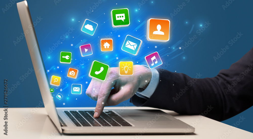 Businessman hand typing on laptop with flying application icons around Businessman hand typing on laptop with flying application icons around