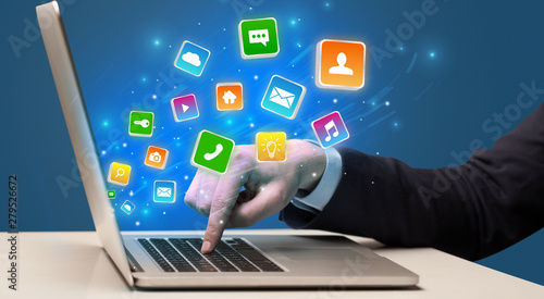 Businessman hand typing on laptop with flying application icons around