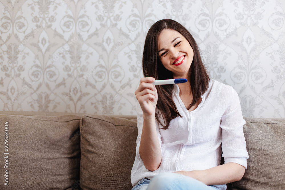 Young woman rejoices while looking at a positive pregnancy test Young woman rejoices while looking at a positive pregnancy test