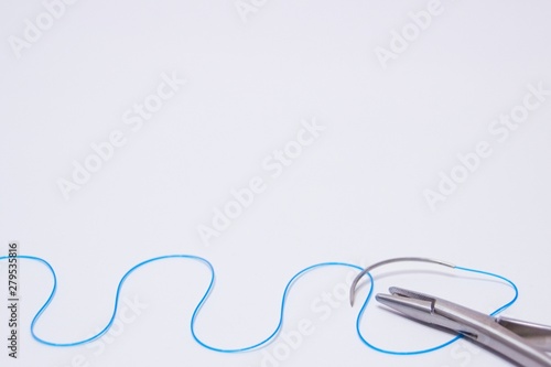 Medical equipment for sewing wounds. The kit includes a needle holder and a needle with surgical suture on a white background with plenty of copy space. Concept of medical care or medical study.