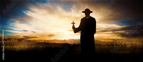 priest on the hill at sunset with the cross