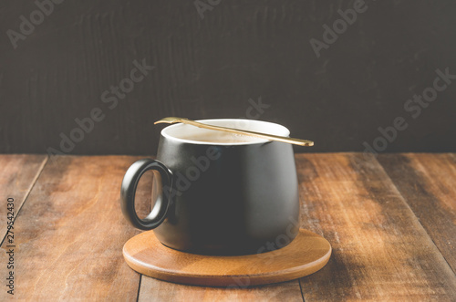 black mug of a cappuccino in a wooden support, on a wooden table