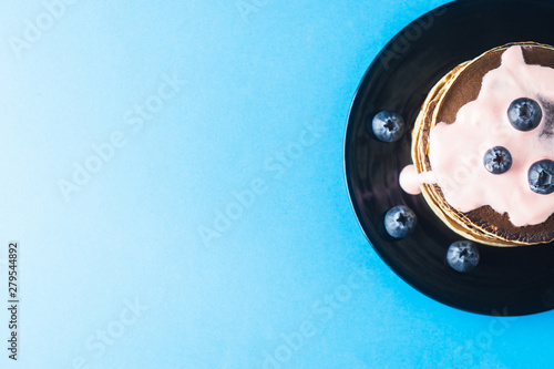 Pancakes with blueberries and syrup on a black saucer on a blue background