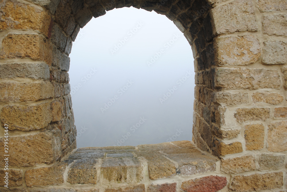 Window of an ancient monastery in the wall, fog